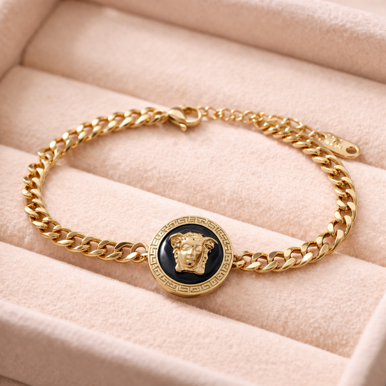 Gold chain bracelet with a black medallion on a beige surface